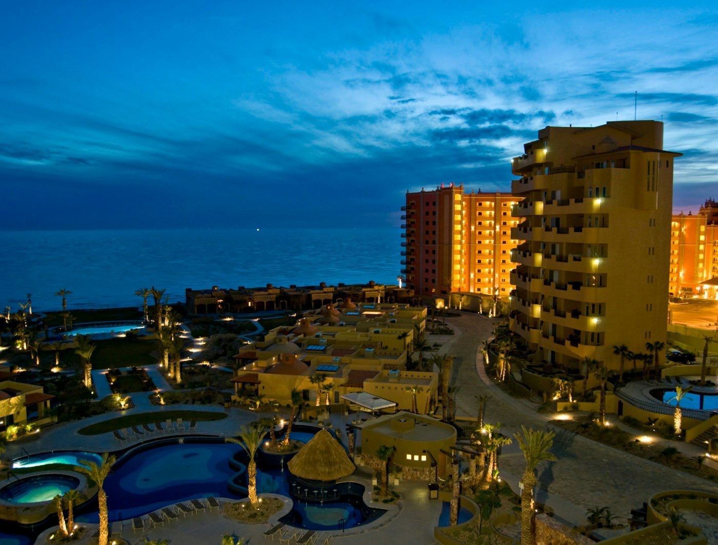 Bella Sirena towers, villas, and lit pools on Sandy Beach at dusk